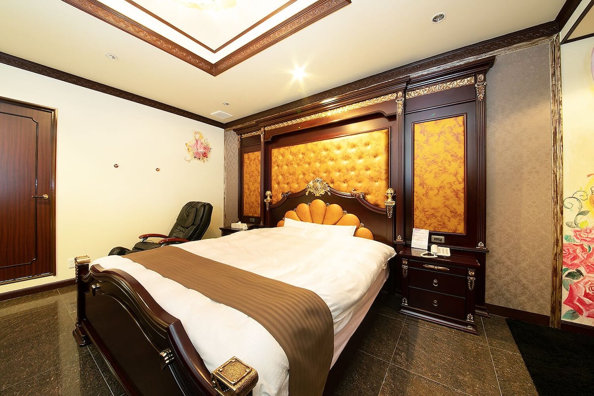 A hotel room with a large bed, a wooden headboard, a nightstand with a telephone, and a chair.