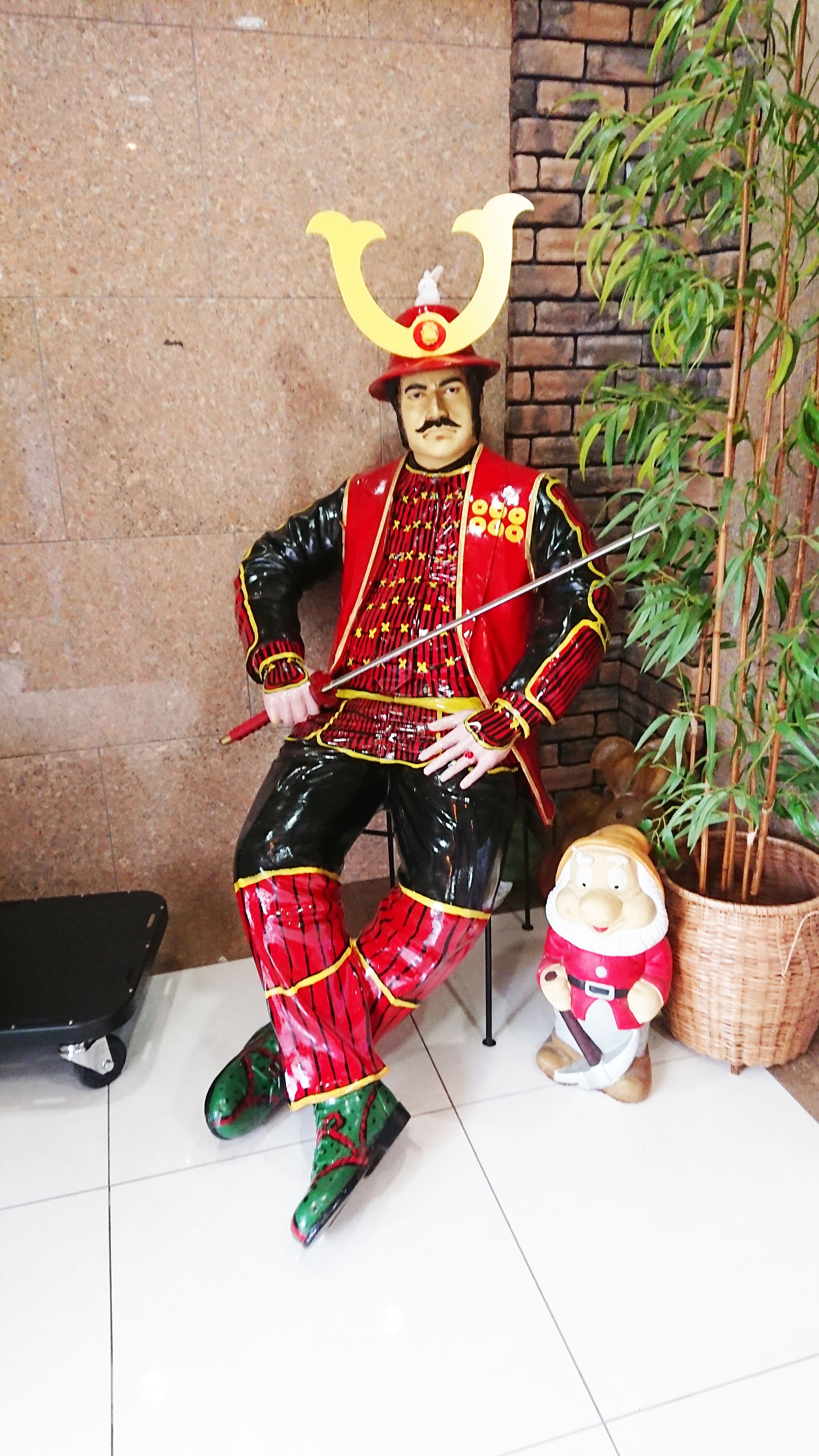 En statue af en figur i traditionelt tøj med hjelm, siddende på en stol.