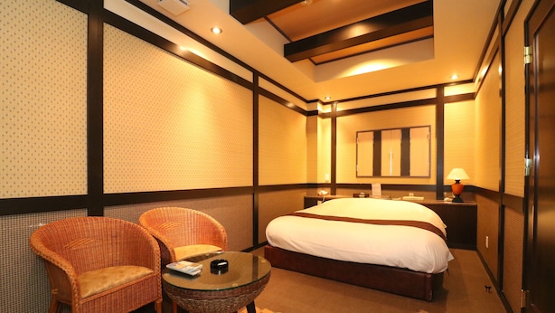 A hotel room with a large bed, two wicker chairs, a small glass table, and a mirror on the wall. - Hotel To (Wakayama)