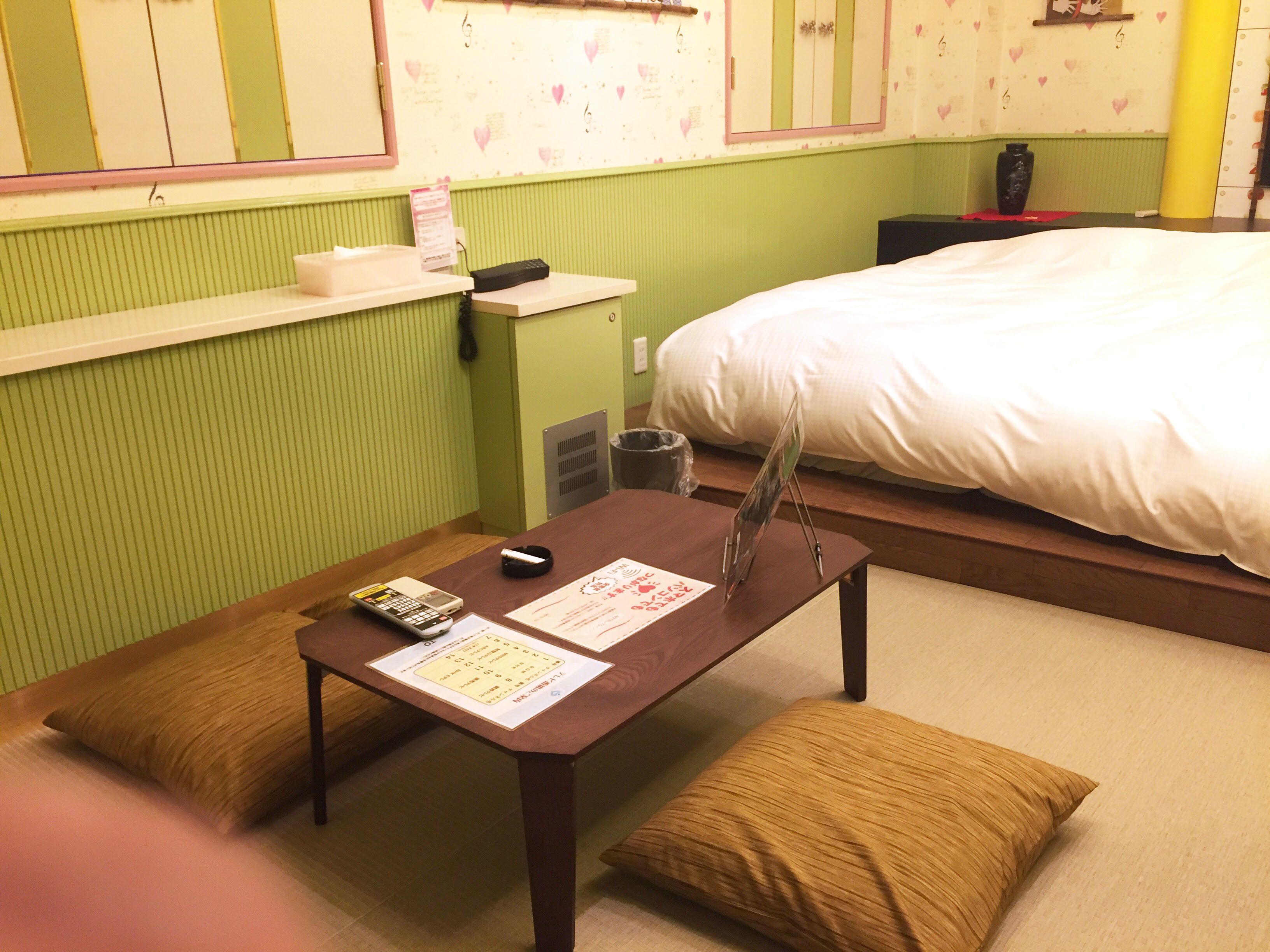A hotel room with a bed, a small table with a remote control, a vase, and a pillow.