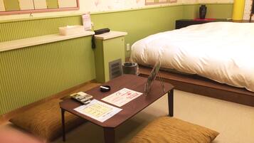 A hotel room with a bed, a small table with a remote control, a vase, and a pillow.