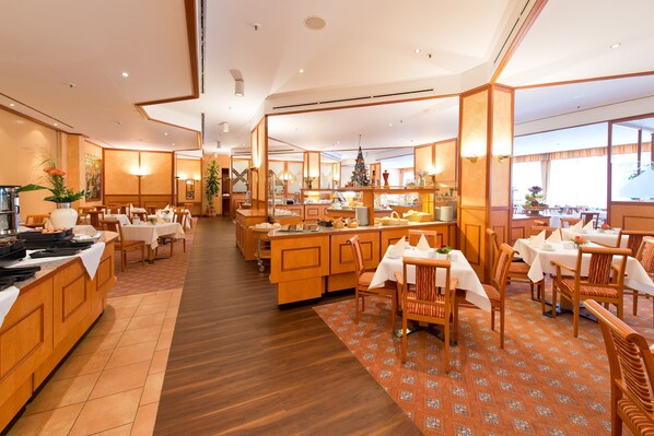 Comedor de hotel con mobiliario de madera, una isla central con un árbol de Navidad y grandes ventanales que ofrecen luz natural.
