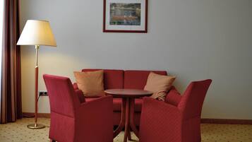 Un rincón de sala con un sofá rojo y dos sillones, una mesita redonda y una lámpara de pie.