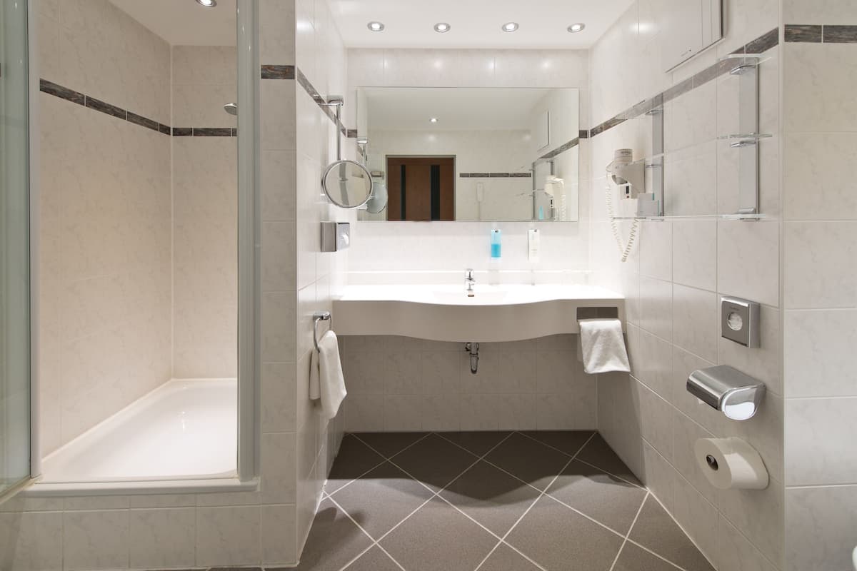 A modern bathroom with a glass-enclosed shower, a white sink with a mirror above, and a towel rack.