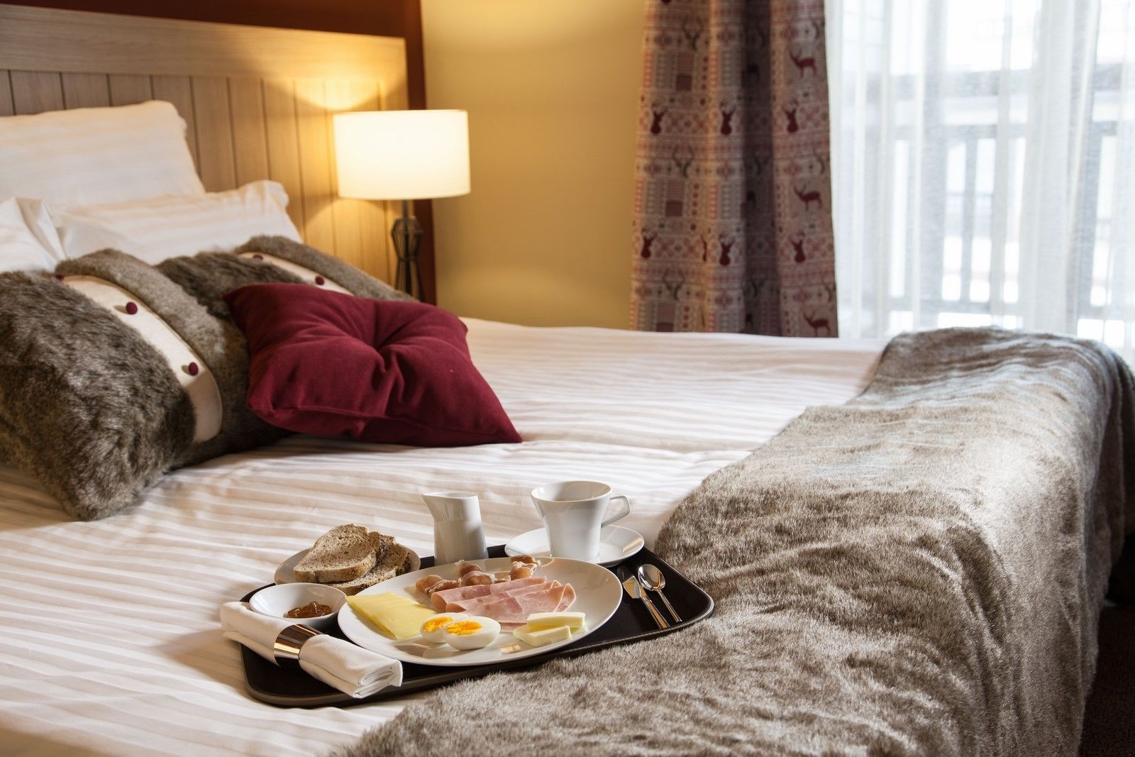 A neatly made bed with a breakfast tray, pillows, and a lamp in a hotel room.