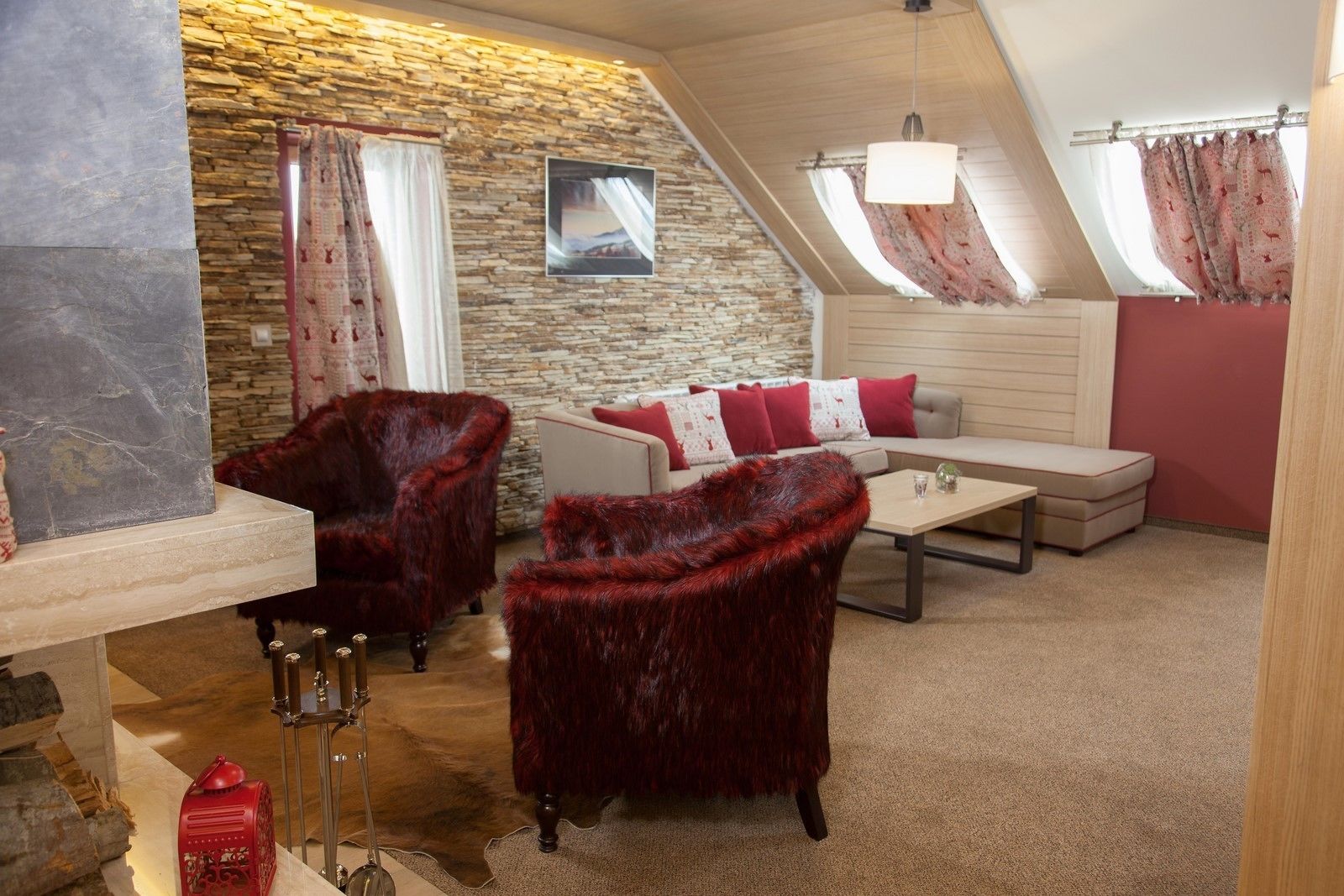 A cozy loft bedroom with a stone wall, a fireplace, a sofa, and a red furry chair.