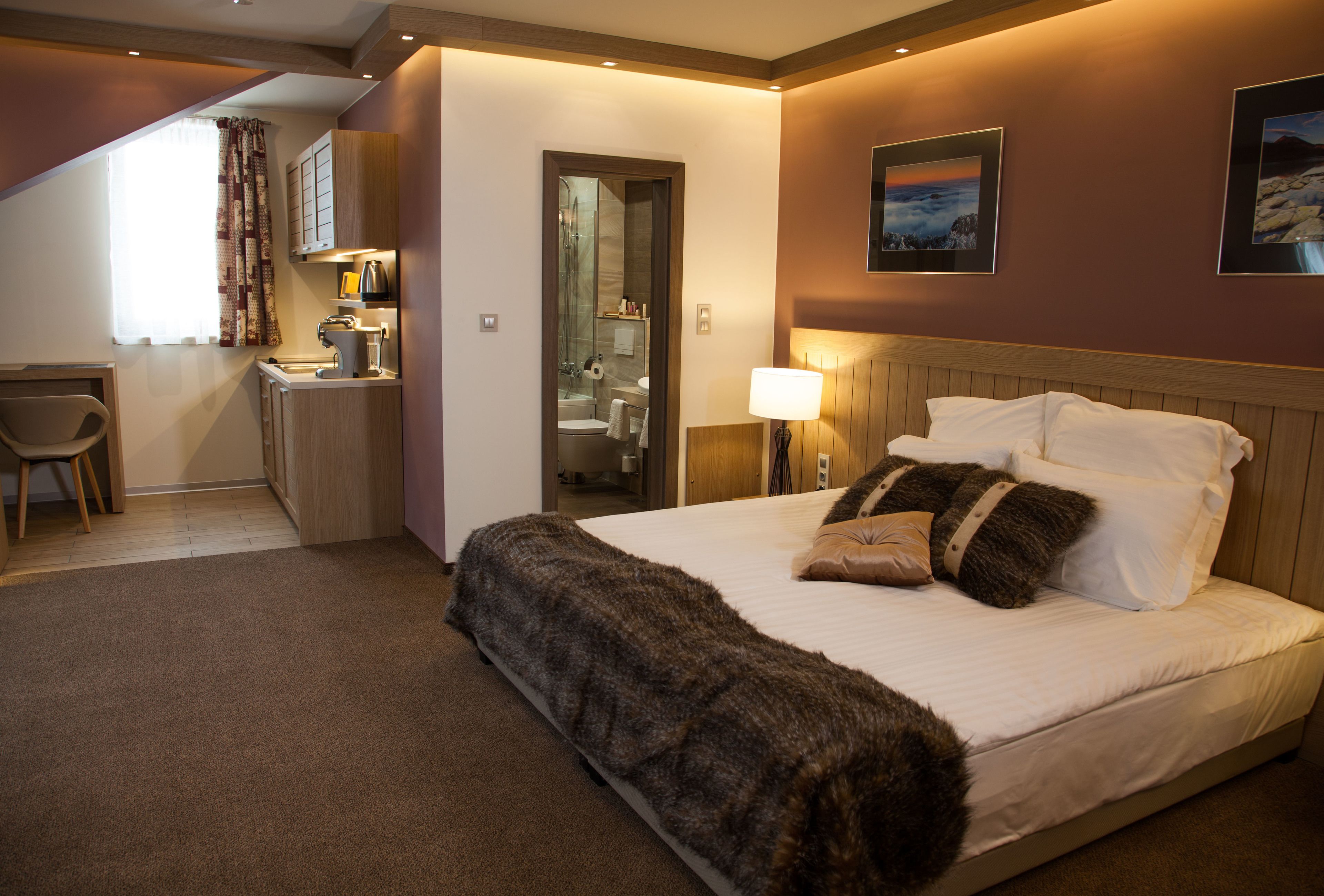 A hotel room with a bed, a desk, a chair, a bathroom, and a view of the outside.