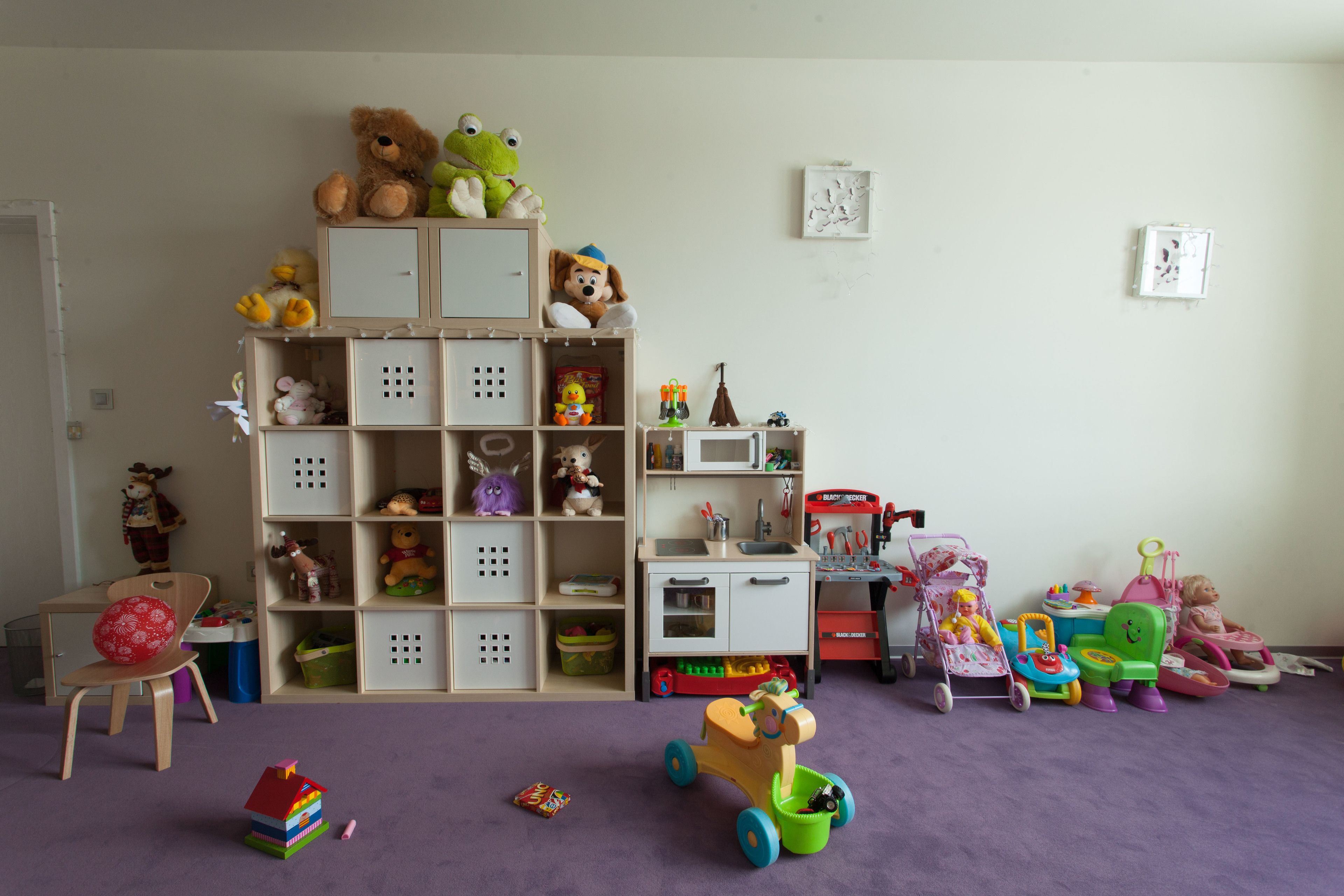 A child's playroom with a wooden toy shelf, a small desk, and a purple carpet.