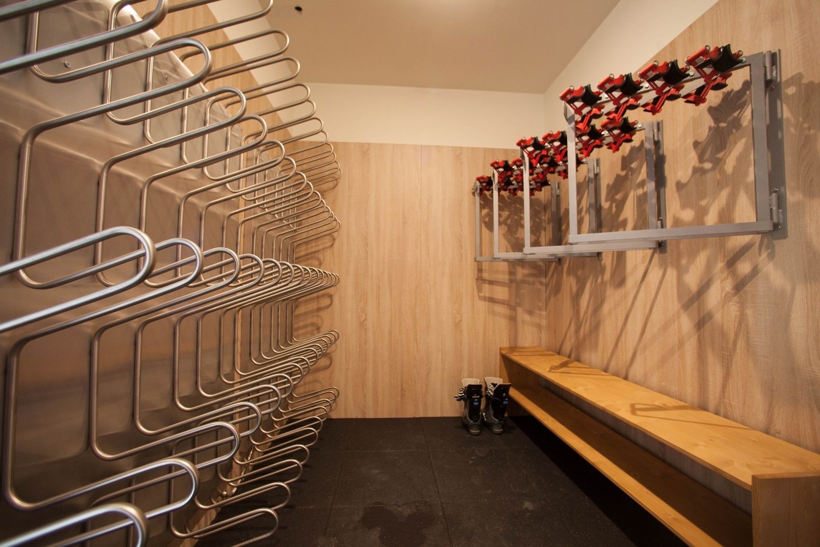 Un baño moderno con toalleros metálicos, un banco de madera y un espejo montado en la pared con adornos rojos.