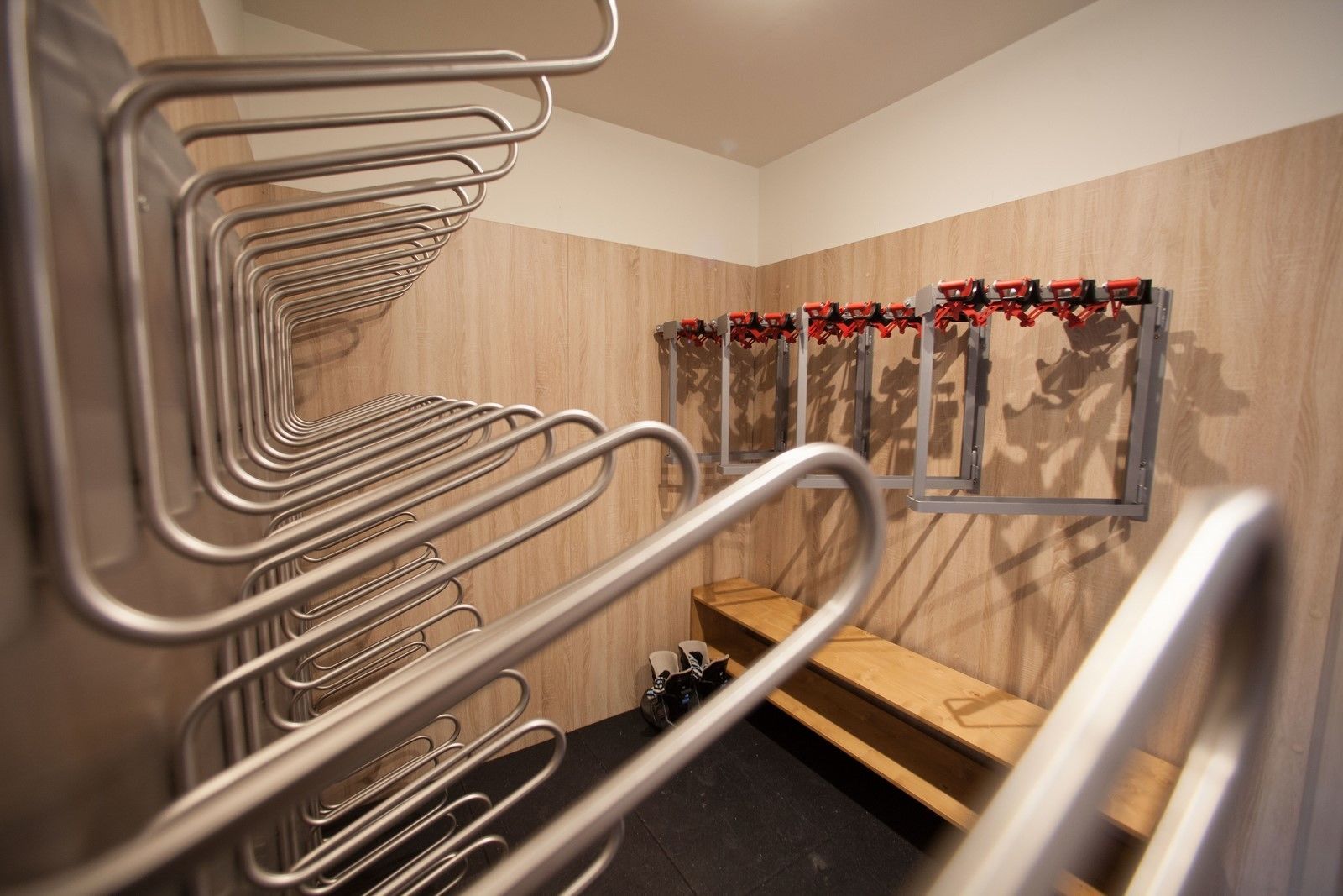 A modern bathroom with metal towel racks, a wooden bench, and a mirror with red decorations.