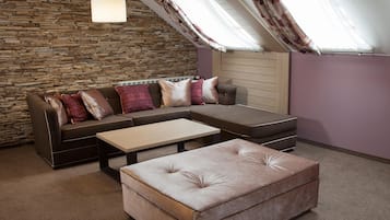 A loft-style room with a stone wall, a sectional sofa with patterned cushions, a small ottoman, and a wooden headboard.