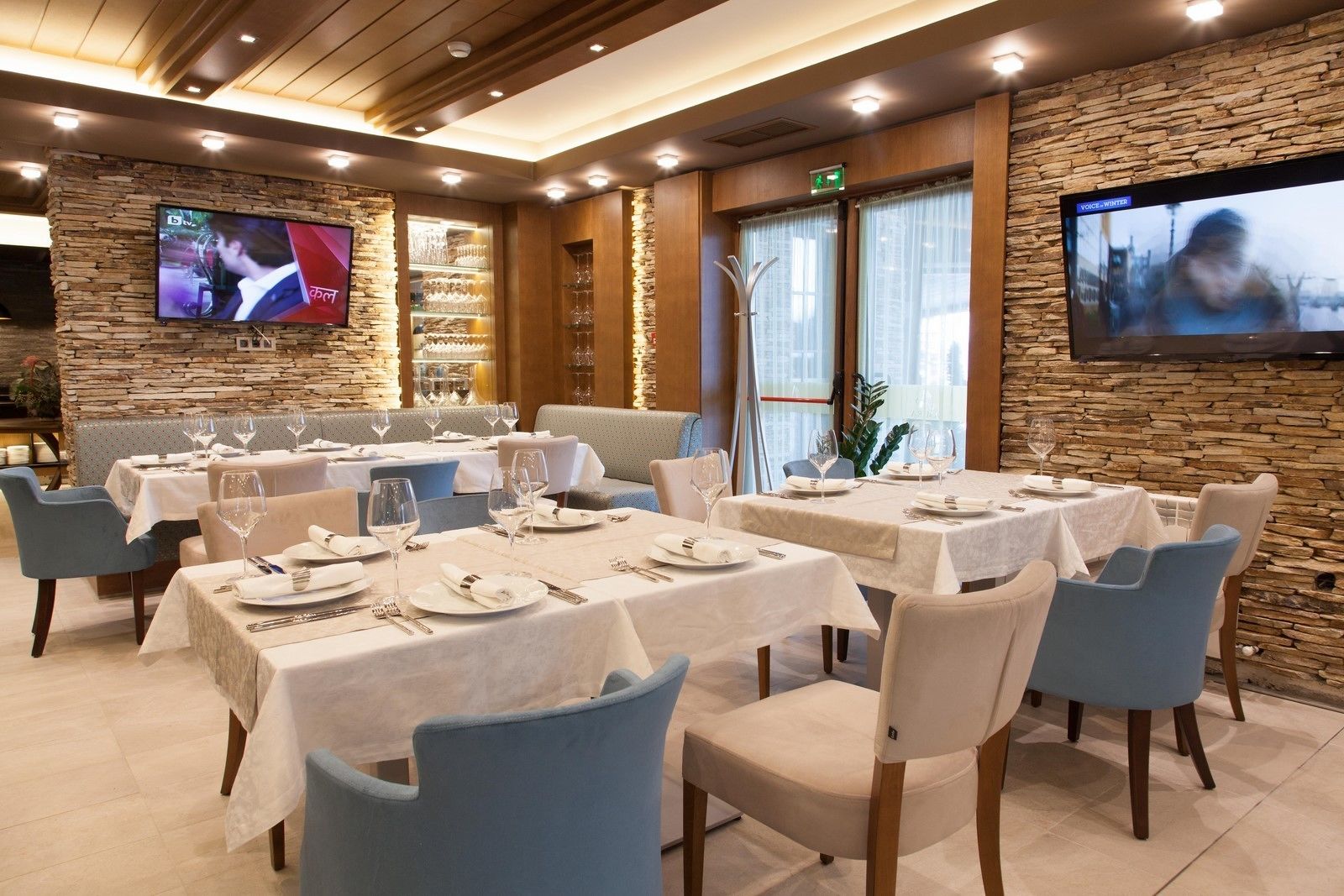 Ein Restaurant mit mehreren gedeckten Tischen, Steinwänden und einem Fernseher, der ein Programm zeigt.