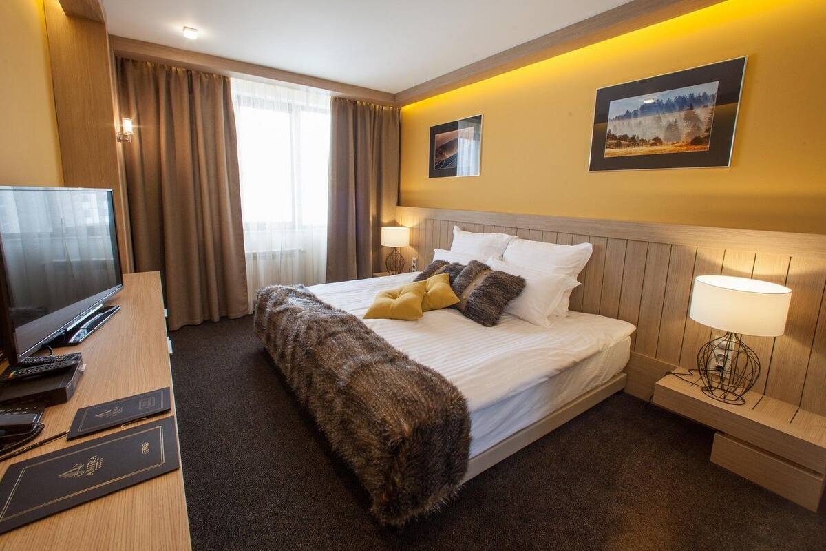A hotel room with a large bed, a desk with a computer and phone, a TV, and two bedside lamps.