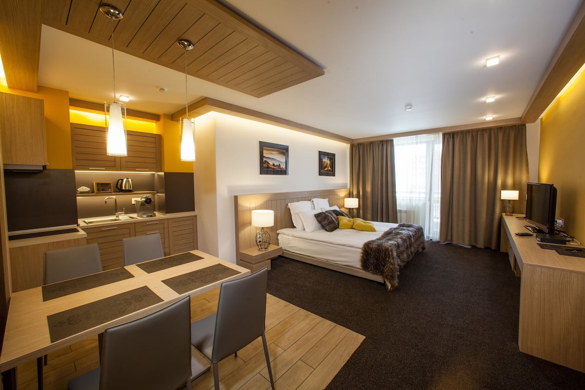 A modern hotel room with a dining area, a bed with a view, and a TV.