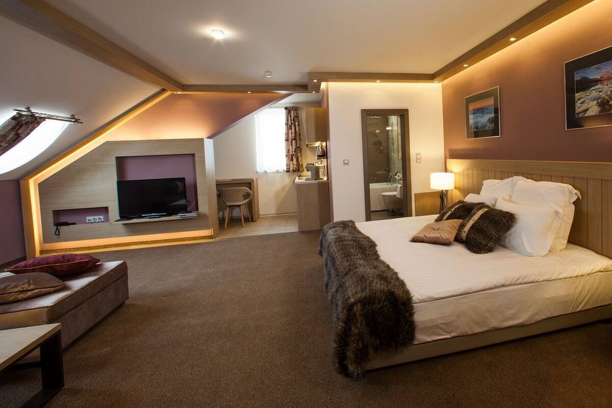 A modern hotel room with a large bed, a TV mounted on the wall, and a cozy seating area with a sofa and a small table.