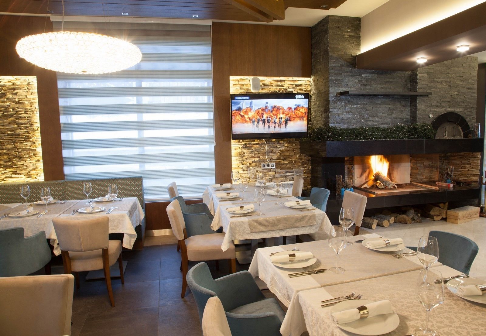 Un restaurante con mesas listas para comer, una chimenea y una pantalla de televisión que muestra un evento deportivo.