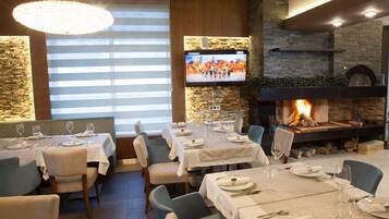 Un restaurante con mesas listas para comer, una chimenea y una pantalla de televisión que muestra un evento deportivo.