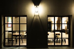 Un pasillo con una lámpara moderna y puertas de cristal que dan a un comedor con mesas y sillas.