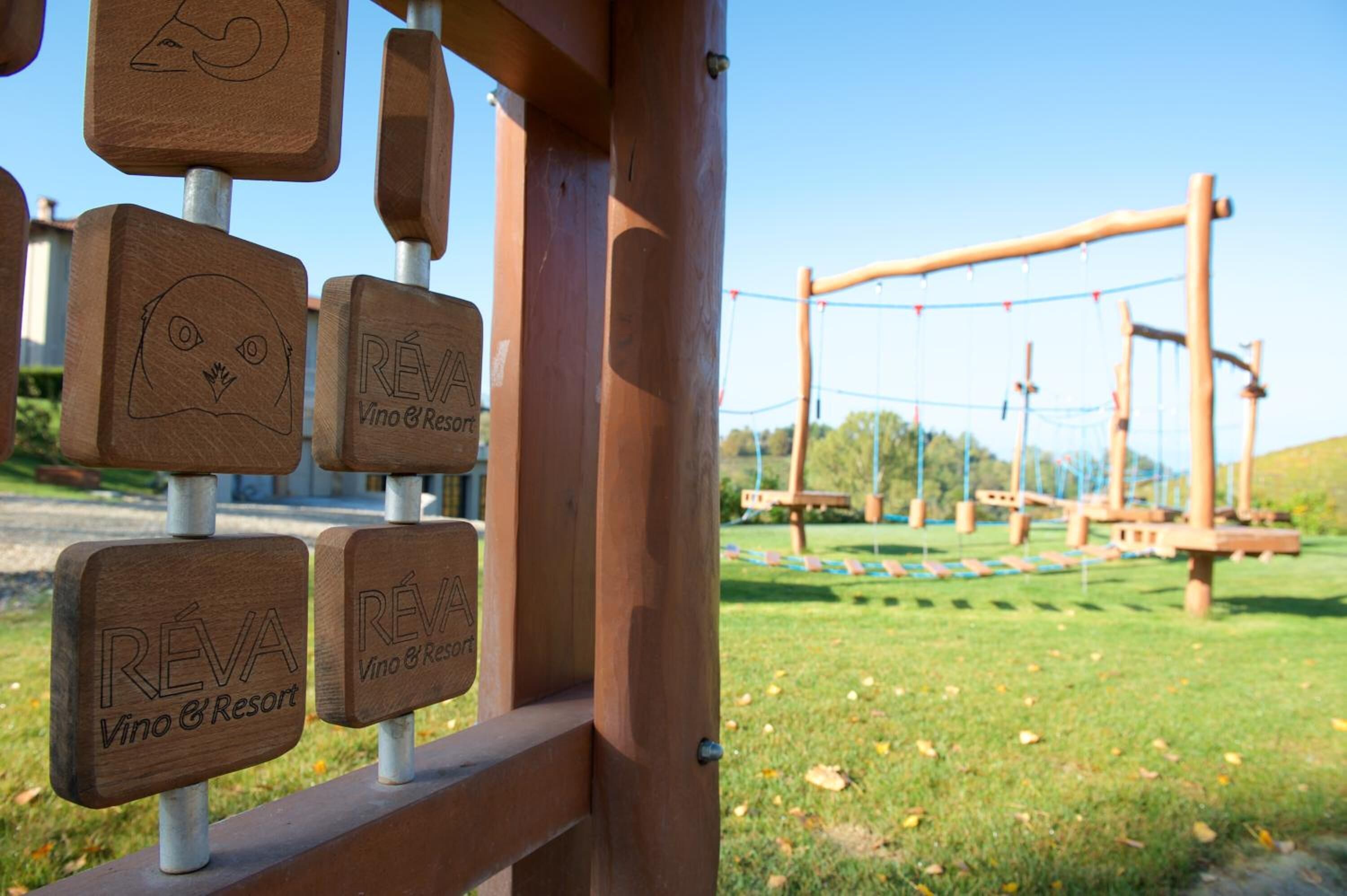 Wooden signs with the logo 'REVA Vino & Resort' and a playground structure in the background.