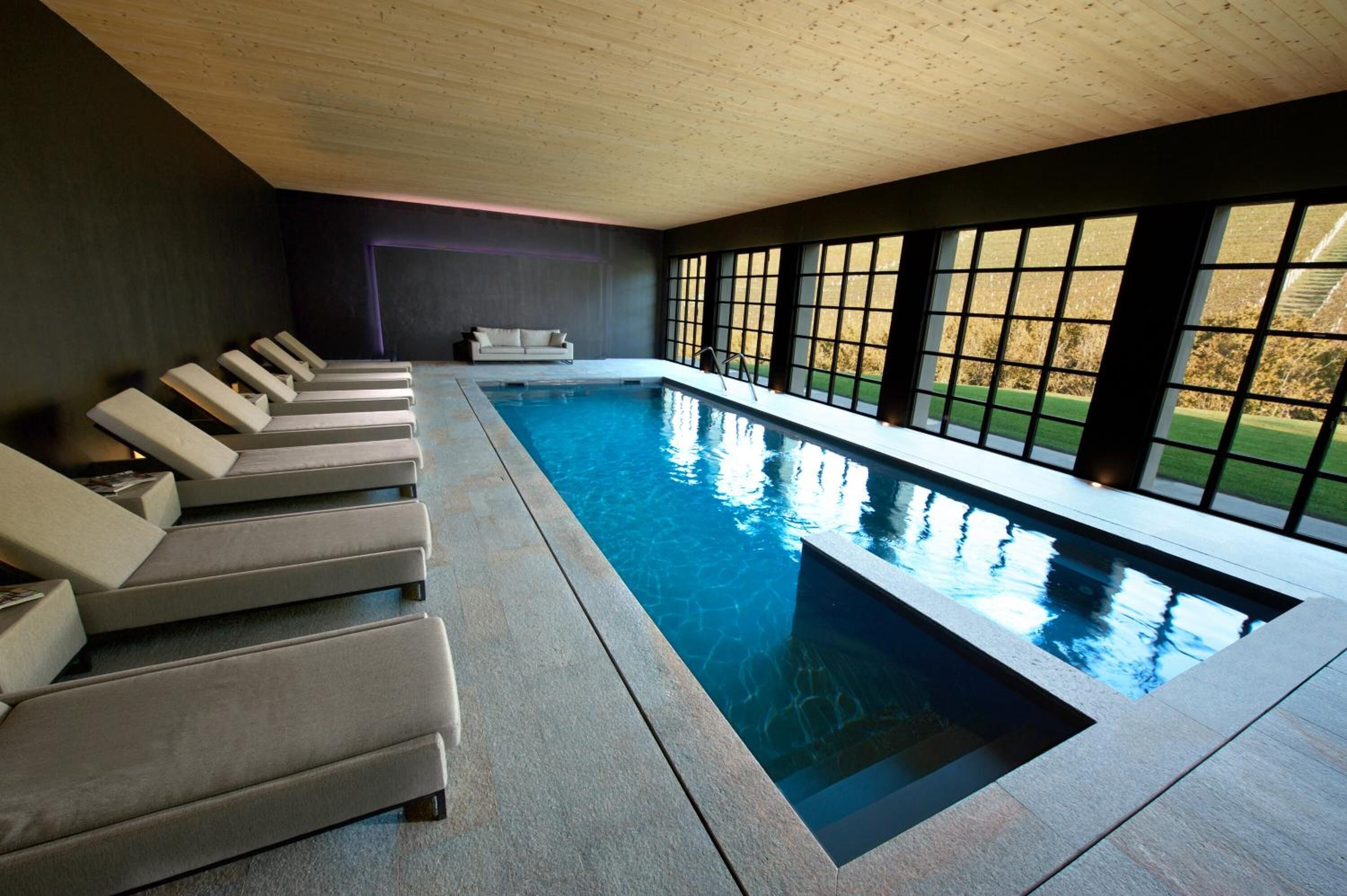 Una piscina interior moderna con múltiples sillas de descanso y ventanas amplias.