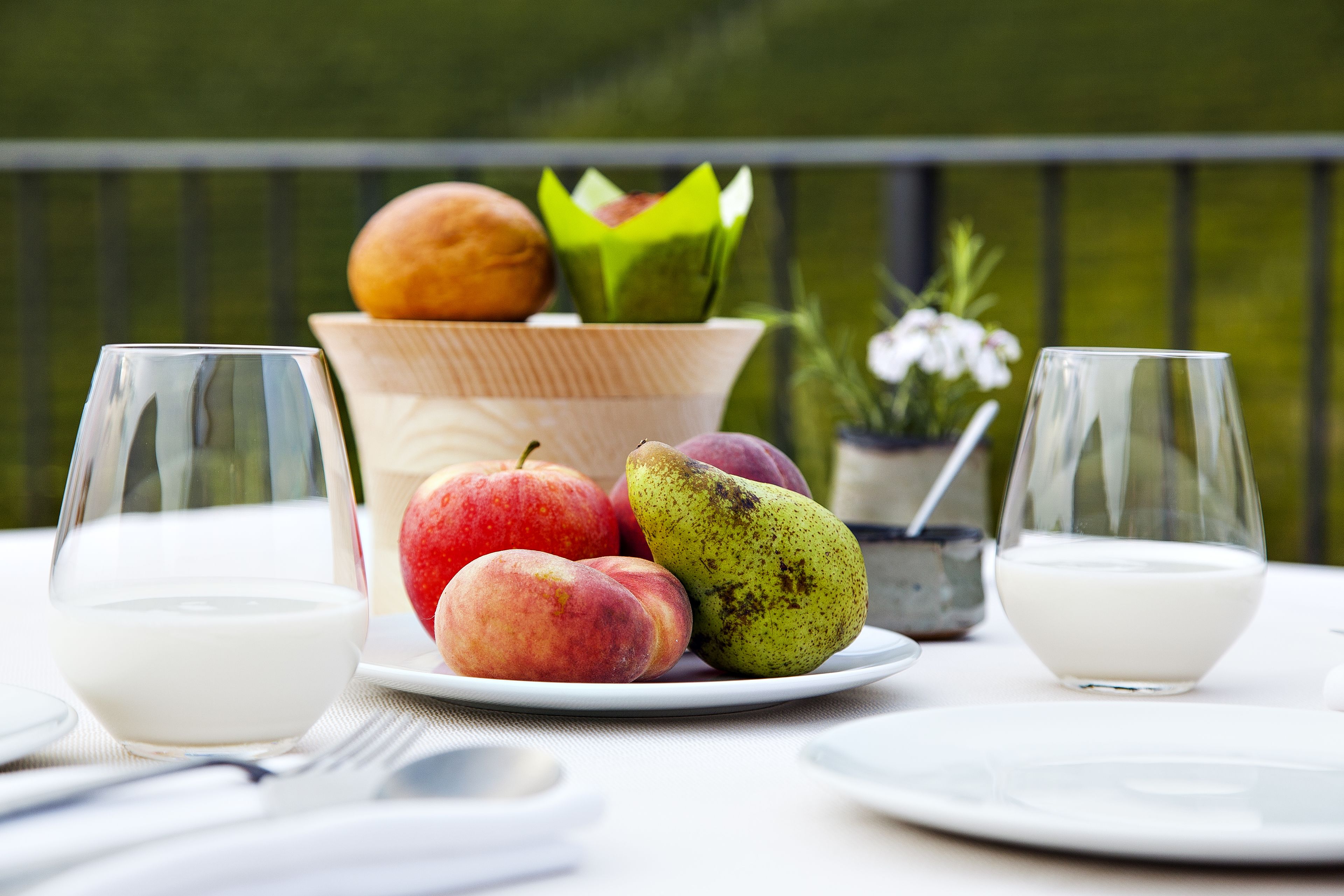 Una mesa de comedor con un plato de fruta, dos vasos de leche y un bol de pan.