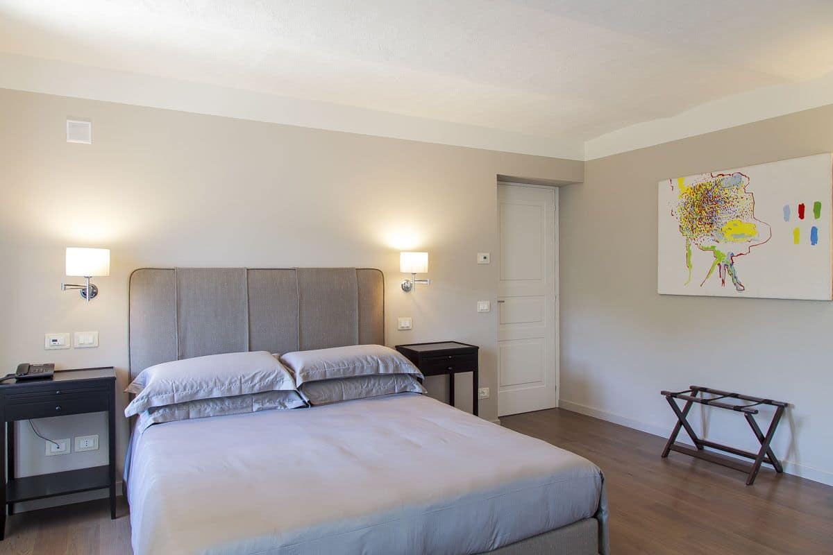 Habitación de hotel con una cama grande, lámparas de noche, una mesita y una obra de arte colgada en la pared.