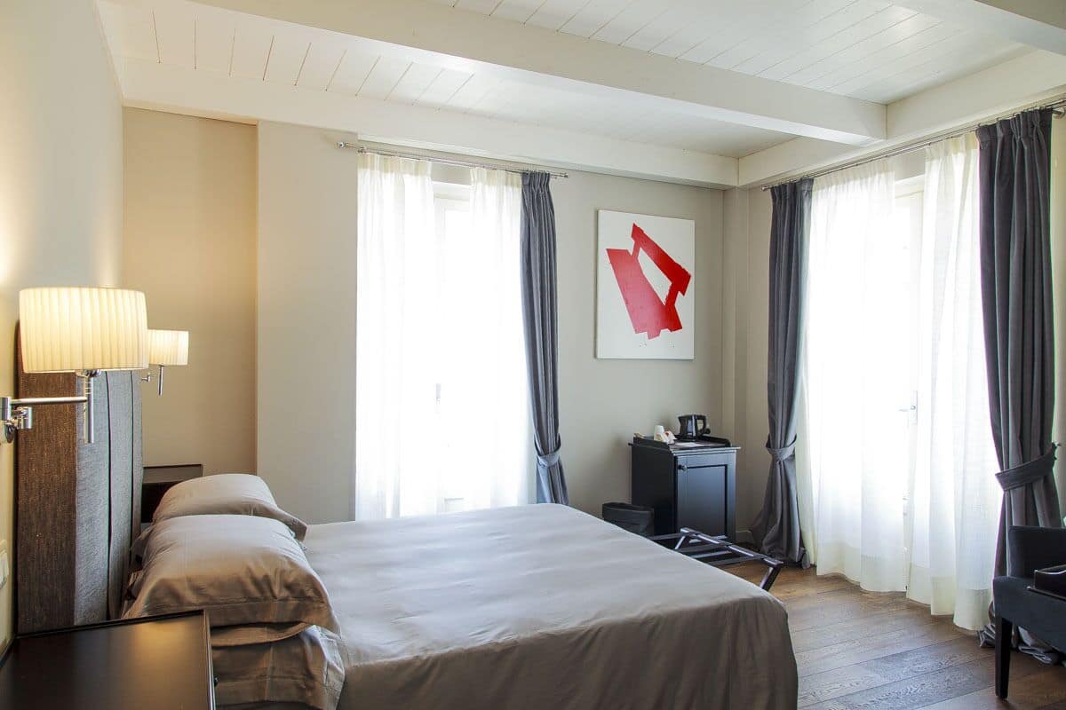 Una habitación de hotel con cama, escritorio, lámpara y un cuadro en la pared.