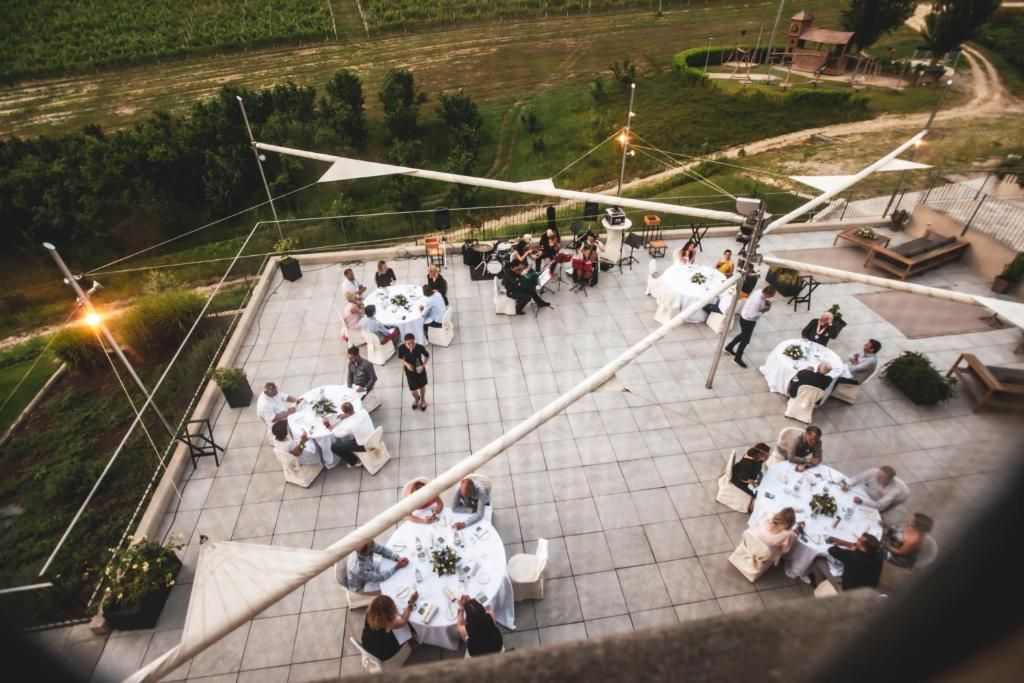 Ein Terrassenbereich im Freien mit mehreren runden Tischen zum Essen, umgeben von Stühlen und Blumentöpfen.
