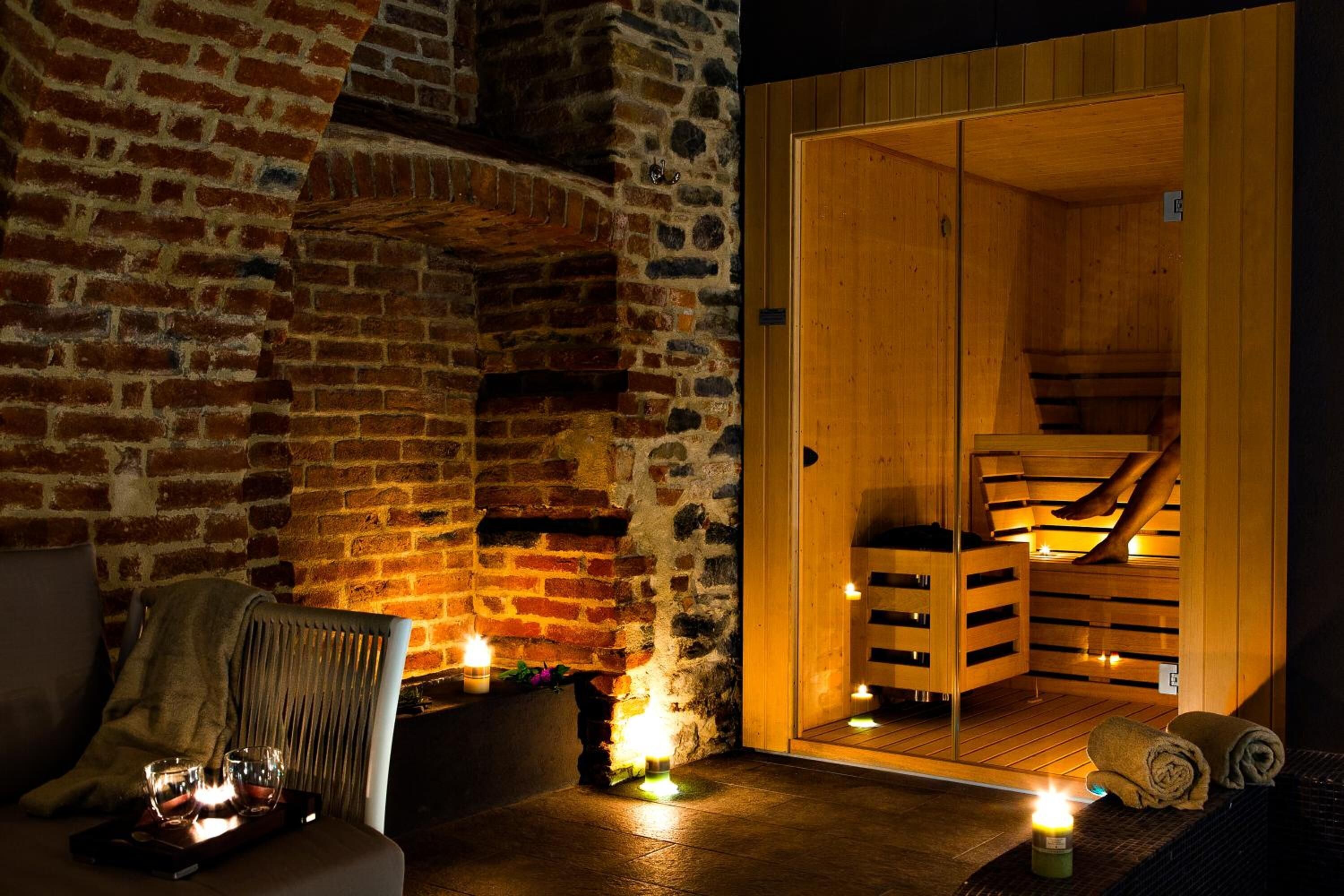 Eine Sauna mit Backsteinwand, Holzsitzen und Kerzen für eine warme Atmosphäre.