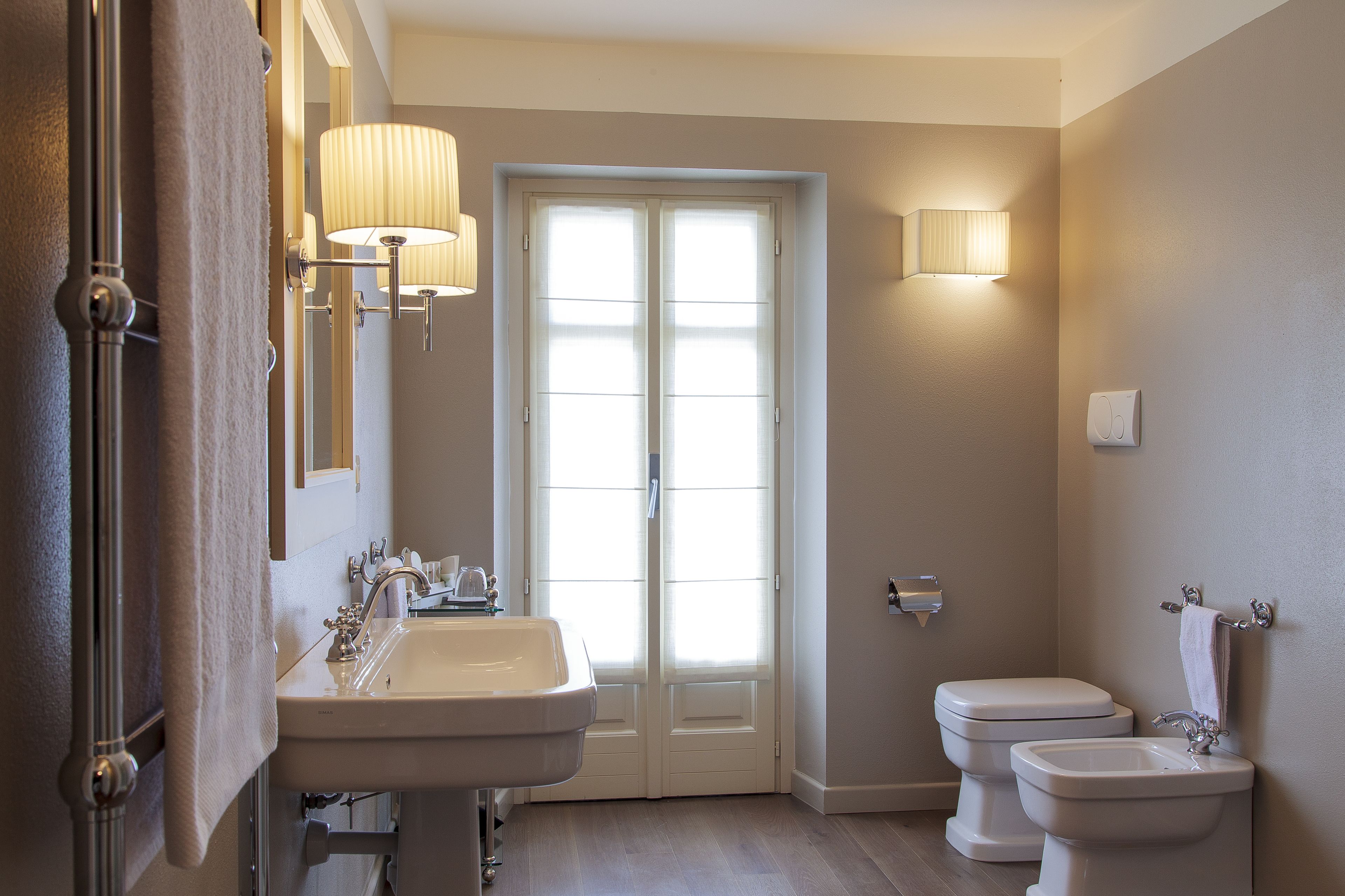 A bathroom with a sink, toilet, and bidet, featuring a double door and wall-mounted lighting.