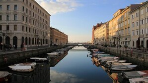 Un canal con barcos amarrados a ambos lados, bordeado por edificios históricos con ventanas de arco y un cielo despejado.