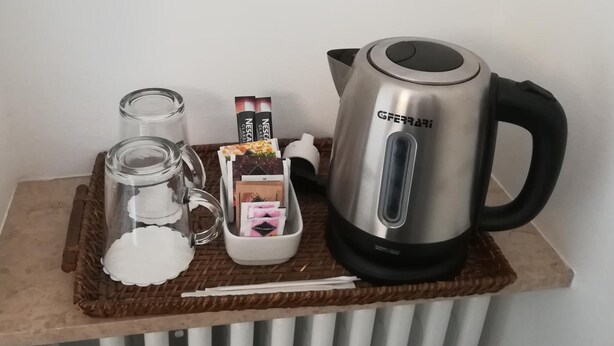Una cafetera Nescafé de acero inoxidable, un frasco de vidrio, una taza blanca y una bandeja de mimbre con cápsulas de café y una cuchara.