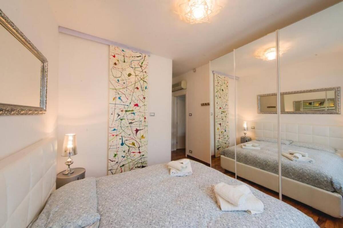 Une chambre d’hôtel avec un grand lit, un miroir et un mur orné d’un motif abstrait aux couleurs vives.