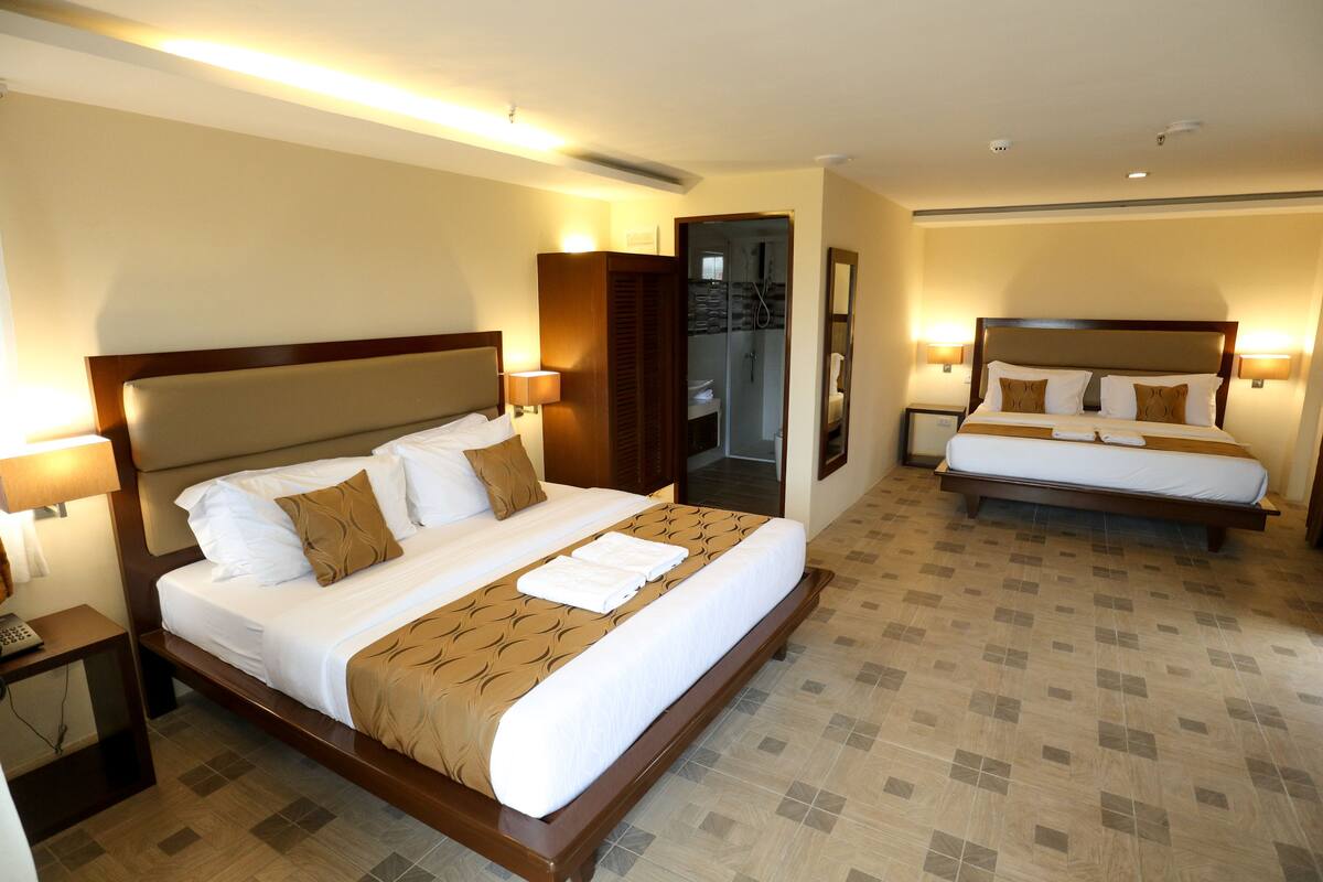 Habitación de hotel con una cama grande, una cama más pequeña, un baño y una mesita de noche con un teléfono.