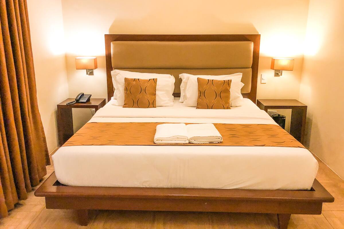 Habitación de hotel con una cama grande, dos mesitas de noche, un teléfono y dos lámparas fijadas a la pared.