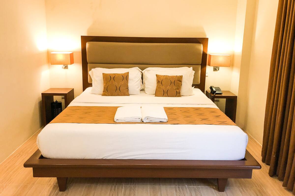 Una habitación de hotel con una cama grande, dos mesitas de noche y un cabecero.