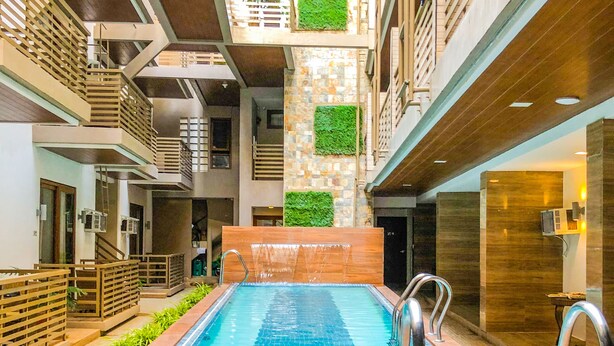 An indoor swimming pool with a tiled floor, surrounded by wooden railings and greenery.