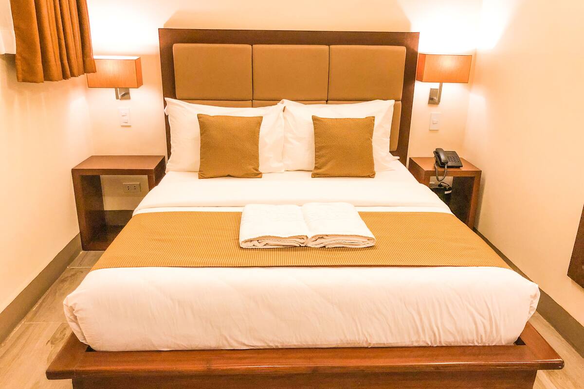 Habitación de hotel con una cama grande, dos mesitas de noche, una lámpara y un teléfono.