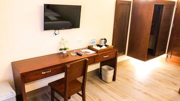 Habitación de hotel con un escritorio de madera, un televisor montado en la pared, una pequeña planta y un cubo de basura.