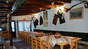A dining area with wooden tables and chairs, a striped tablecloth, and various wall decorations including animal skins and a painting. - Trenchova Guest House (Bansko)