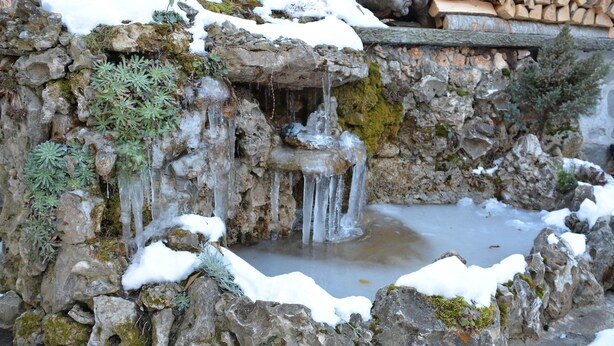 A natural rock formation with a small waterfall and a pond, surrounded by snow and greenery. - Trenchova Guest House (Bansko)