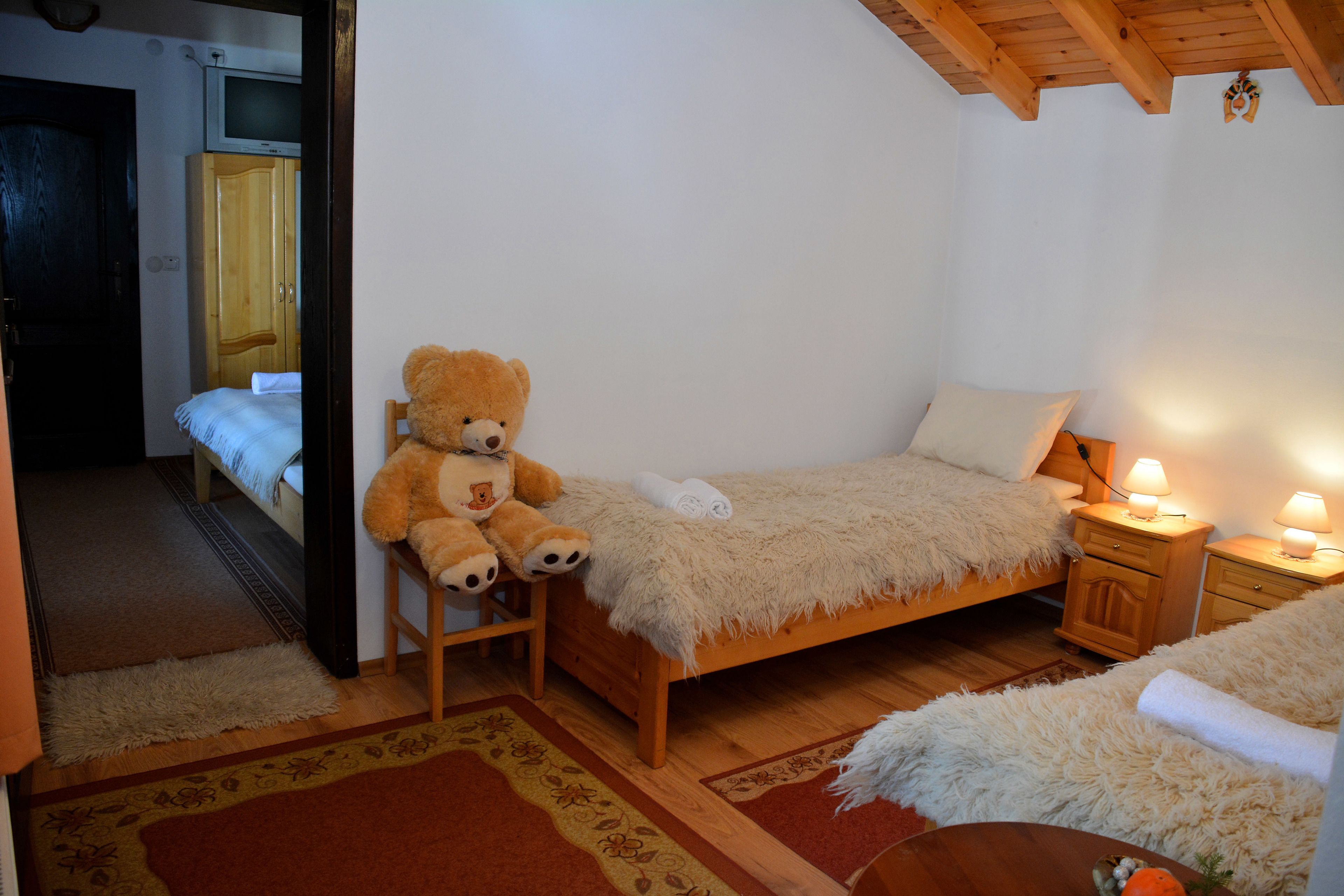 Un dormitorio acogedor con una cama de madera, un oso de peluche, un televisor y una mesita de noche con una lámpara.