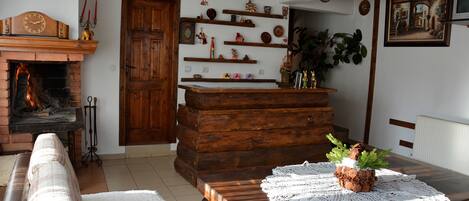 Un salon chaleureux avec une cheminée, des étagères en bois, une table à manger recouverte d’une nappe en dentelle et un canapé.