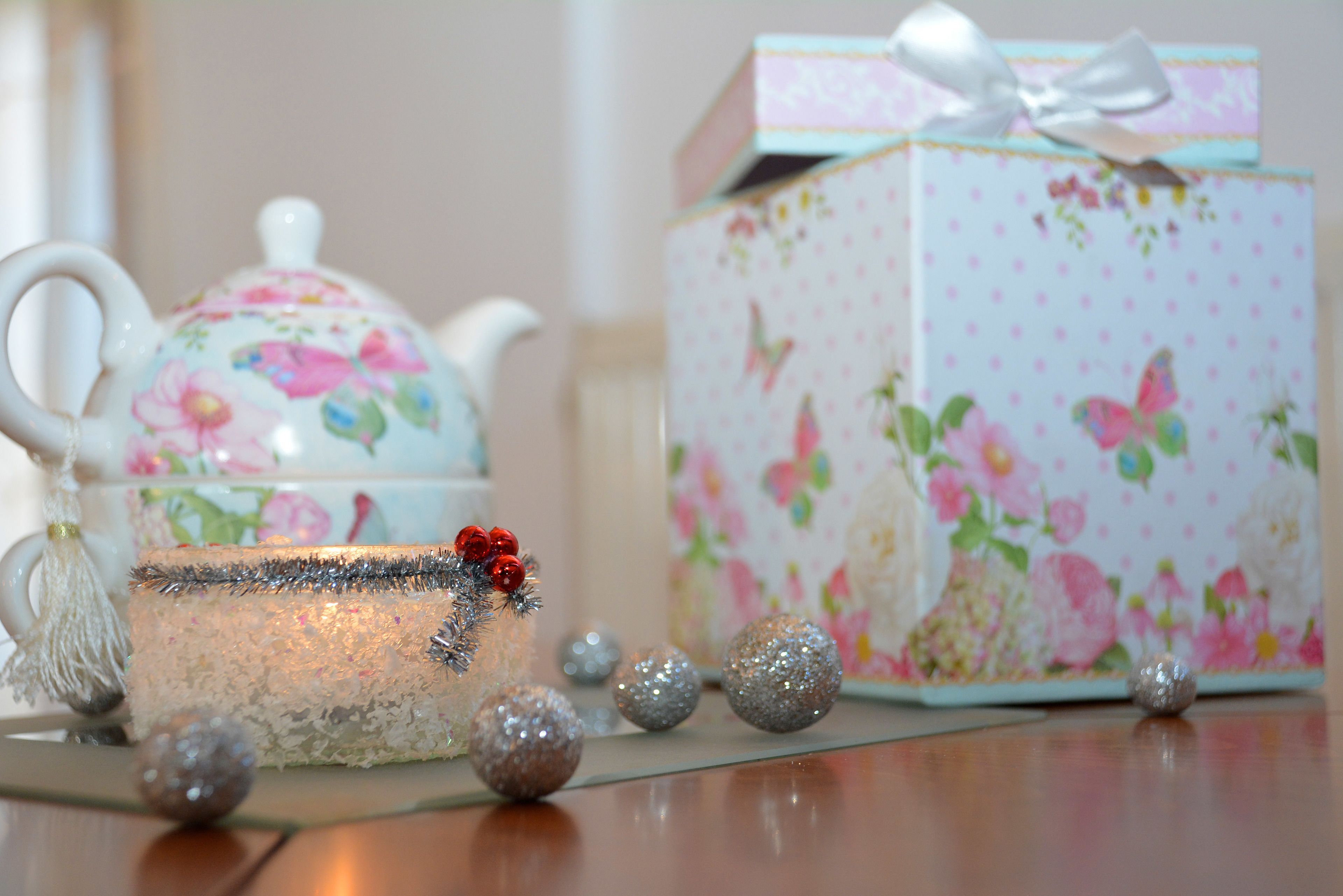 A floral-patterned teapot and box set on a table with decorative balls and a tassel.