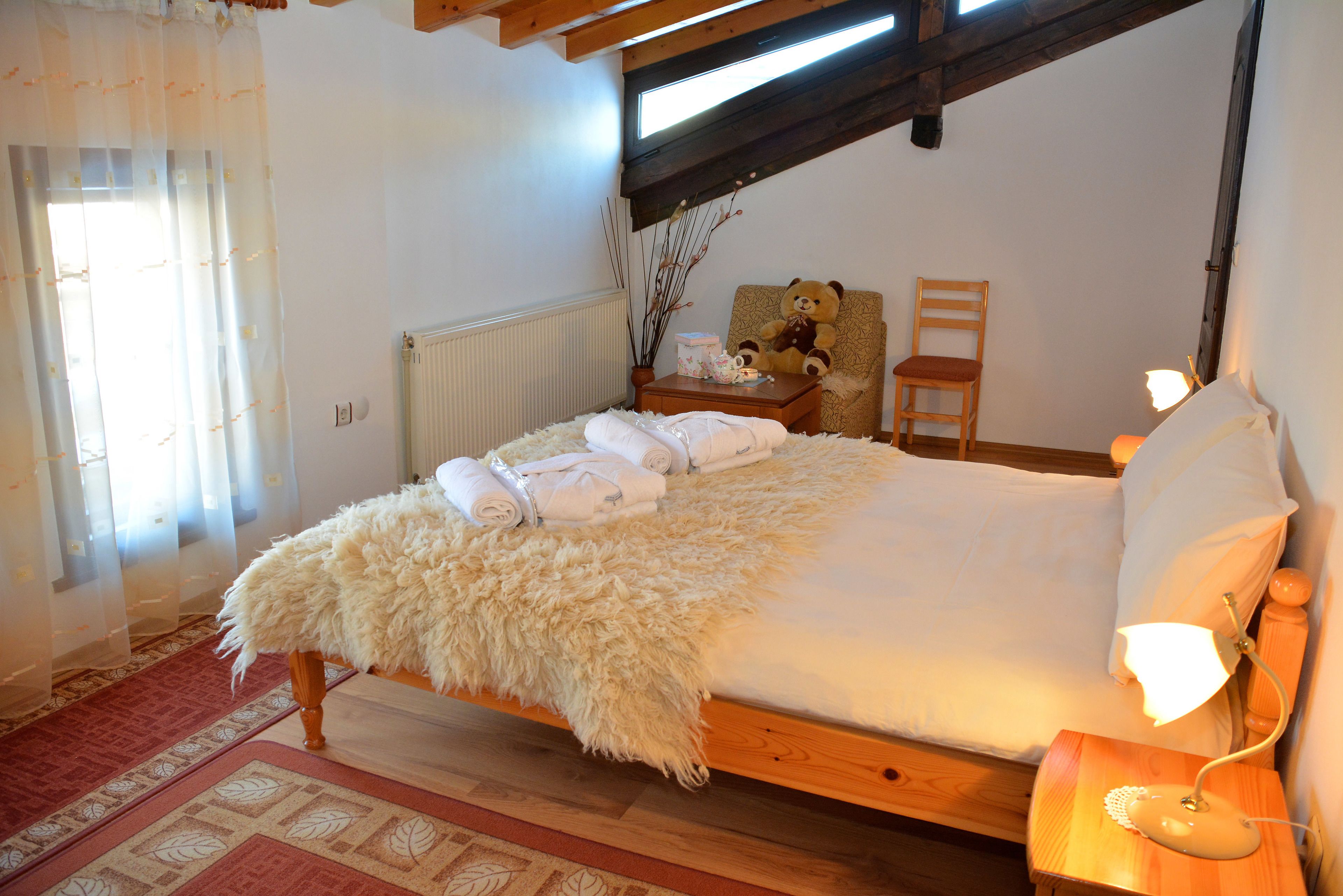 A bedroom with a wooden bed, a nightstand with a lamp, a chair, and a teddy bear.