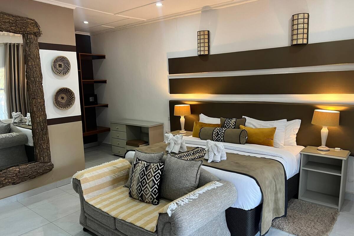 Een moderne slaapkamer met een groot bed, nachtkastjes, een bank en een spiegel.