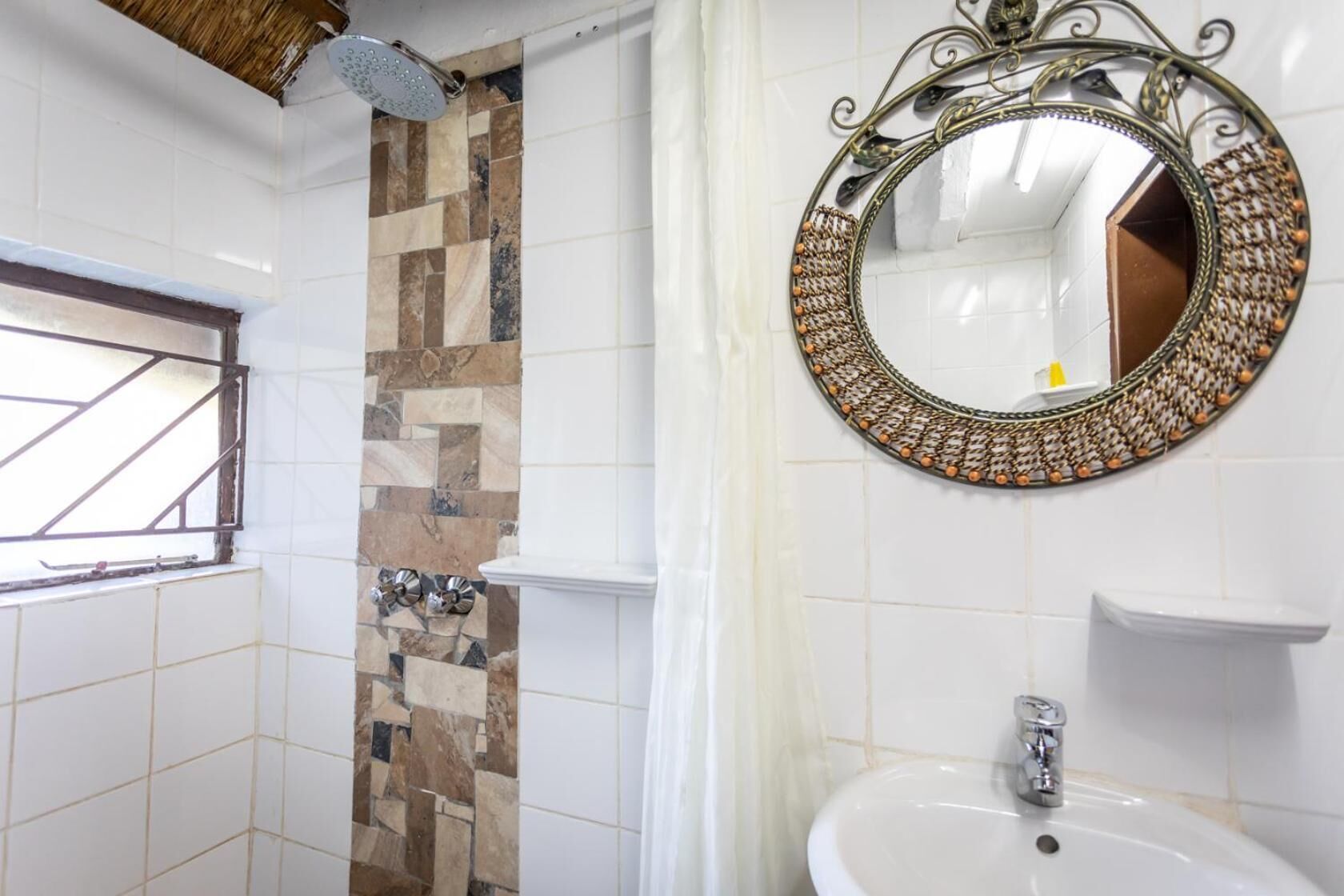Ein Badezimmer mit Dusche, einem Zier-Spiegel und einer gefliesten Wand.