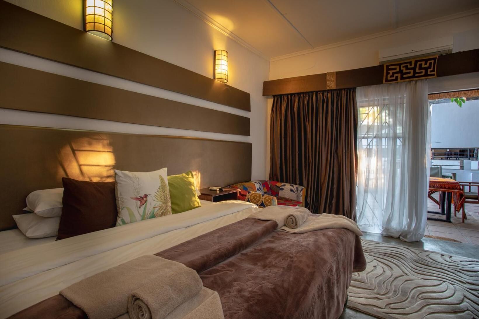 Ein Hotelzimmer mit einem großen Bett, zwei Nachttischlampen, einem Kopfteil und Blick auf die Außenterrasse.