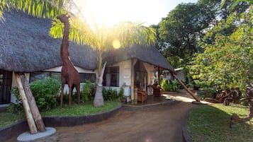 A thatched-roof building with a garden path leading to it, surrounded by tropical plants and a giraffe statue.