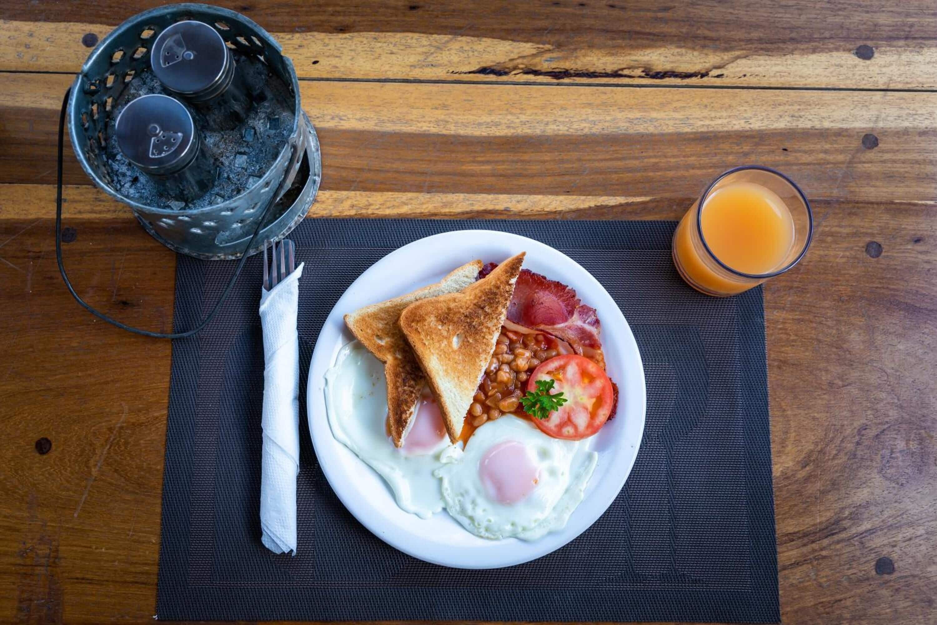 Un plato de desayuno con tostadas, huevos, frijoles y tomate sobre una mesa de madera.